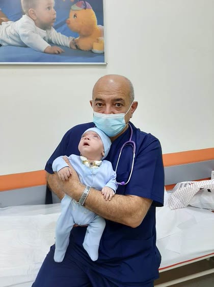 Dr. Sahib Cəfərov müayinədən sonra körpəni qucağında tutur
